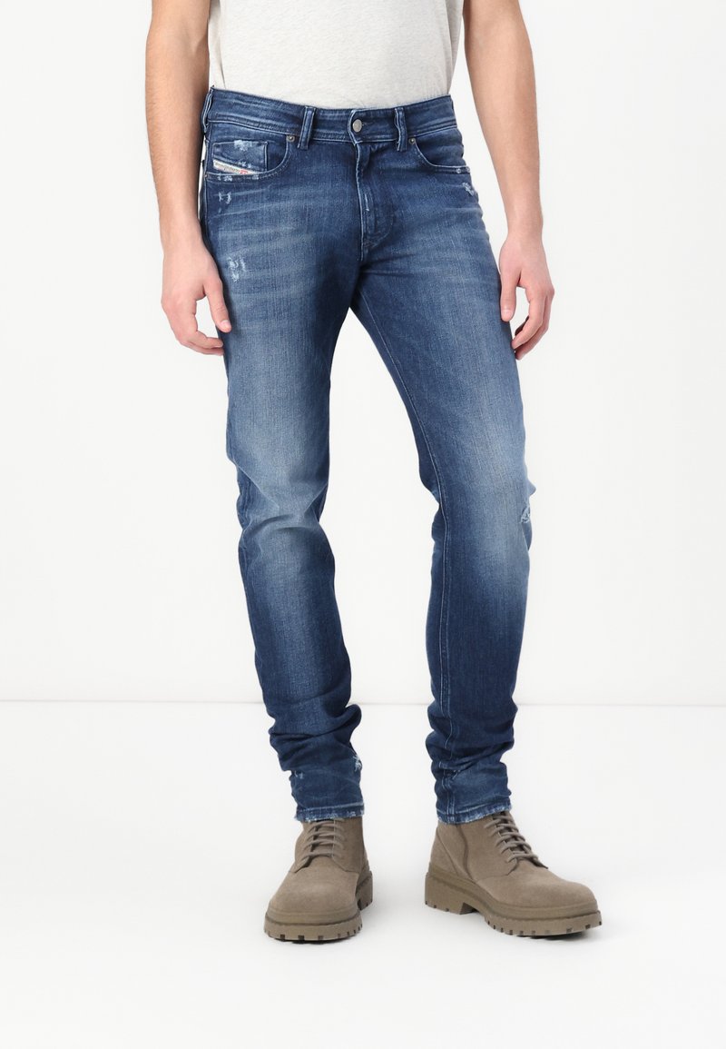 Μαύρες τζιν παντελόνες από κανονικό ύφασμα με στενή εφαρμογή, που διαθέτουν ελαφρές φθορές, πέντε τσέπες και κλείσιμο με κουμπί. Φοριούνται με καφέ δερμάτινα μποτάκια με κορδόνια.