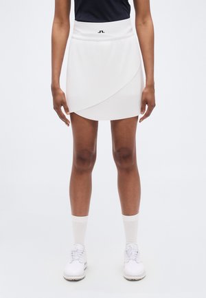 White sports skirt featuring a wrap design, smooth texture, and a high waistband with a small logo accent. Worn with white shoes and socks.