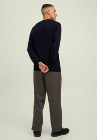 Maglione a maniche lunghe blu navy con collo a giro, abbinato a pantaloni grigi larghi e scarpe nere, visto da dietro.