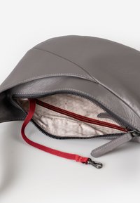 Grijze leren hoes met zwarte rits die gedeeltelijk open is en een beige patroon aan de binnenkant onthult, met een rode stoffen trekband met metalen clip.