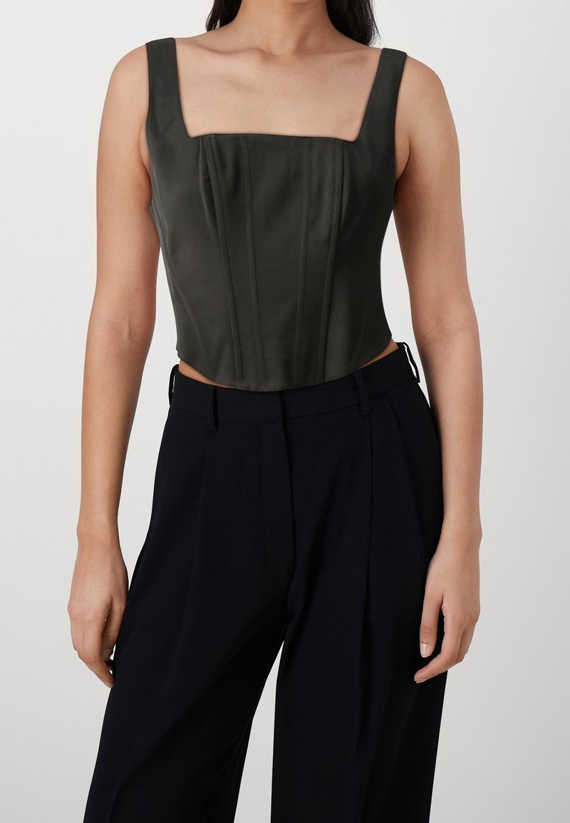 Haut court en satin vert foncé sur mesure avec décolleté carré, bretelles larges et panneaux structurés. Associé à un pantalon noir taille haute.