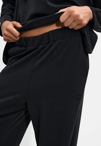 Black loungewear set featuring a relaxed-fit top and pants. The pants have an elastic waistband and subtle stitching detail on the side.