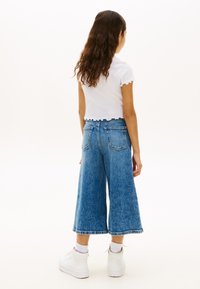 Culottes en denim bleu clair avec une coupe ample et raccourcie. Elles présentent une taille haute, des poches arrière, et un ourlet effiloché. Portées avec un haut blanc à bord festonné.