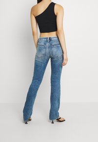 Svart enaxlad croppad topp med blå denim byxor med utsvängda ben, som har blekta områden och en dragkedja i ryggen. Svarta klacksandaler.