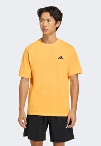 Kurzärmeliges orangefarbenes T-Shirt aus Baumwollmischung mit Rundhalsausschnitt und einem schwarzen Adidas-Logo auf der linken oberen Brust.