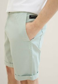 Jasnozielone szorty o gładkiej fakturze, z bocznymi kieszeniami, podwiniętym wykończeniem i czarną metką na pasku.