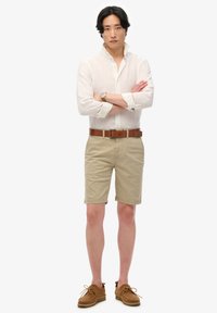 Lichte linnen button-up shirt, kaki shorts, bruine leren riem en tan suède schoenen. Eenvoudig design met opgerolde mouwen en rechte pasvorm.