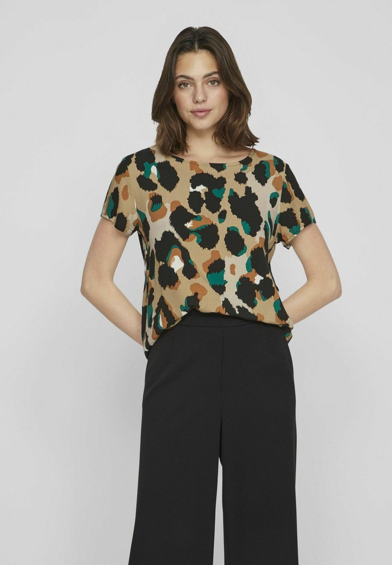 Top a maniche corte con stampa leopardata nei colori marrone, nero e teal su sfondo beige, abbinato a pantaloni neri a gamba larga.