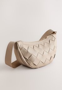 Beige vävd konstläderväska med en rundad form, dragkedjestängning och justerbar tygrem. Har en rutliknande textur och subtil sömnad.