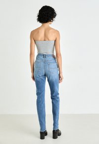 Jeans in denim azzurro chiaro con una vestibilità alta in vita, design a gamba stretta e tasche posteriori distintive. Abbinati a stivaletti neri con zeppa.