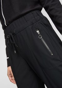 Zwarte joggingsbroek met een elastische tailleband en verstelbaar trekkoord. Voorzien van een ritssluitingzak en een gladde, lichtgewicht stoftextuur.