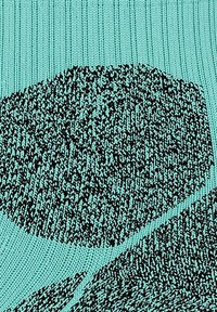 Dzianina w jasnym niebieskim kolorze z teksturowanym geometrycznym wzorem w czerni, zawierająca nieregularne kształty oraz różną grubość nitek dla uzyskania głębi.