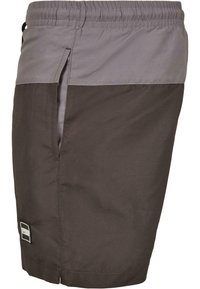 Kurze braune Shorts mit einem grauen Bund, seitlichen Taschen, einer glatten Textur und einem Logo-Patch am unteren Saum.