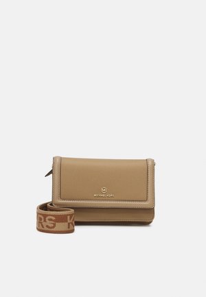 Beżowa torebka Michael Kors na ramię z klapką i regulowanym paskiem materiałowym z nadrukiem logo na jednolitym jasnym tle.