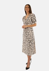 Vestito midi floreale in crema e nero con scollatura a V, maniche a palloncino e spacchi laterali, abbinato a tacchi alti neri.