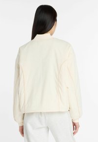 Lichtbeige bomberjack met een hoge kraag, ribbelmanchetten en een zachte textuur. Bevat contrasterende stiksels langs de naden en heeft een relaxte pasvorm.