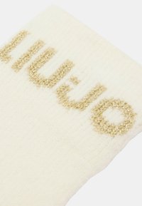 Calzini color crema con texture a coste, con testo ricamato in filo dorato "LIUJO." Materiale in maglia morbida con un design casual.