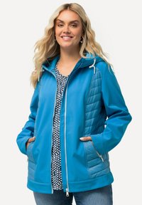 Ljusblå jacka med quiltad textur på sidorna, huva, dragkedjefickor och justerbar dragsko. Bärs över en prickig topp.