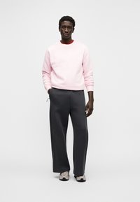 Sweatshirt rosa claro, calças largas cinzentas e ténis bege. A sweatshirt tem um decote redondo e punhos canelados. Design minimalista.