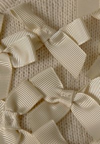 Krämfärgad texturerad tyg med flera ljusbeige satinband arrangerade i rosetter, som visar en slät yta och subtil lyster.