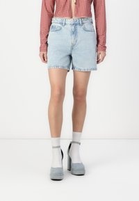 Shorts en denim bleu clair avec un ourlet effiloché, dotés d'un design à cinq poches et d'une fermeture à bouton à l'avant, associés à des chaussures à plateforme grises et des chaussettes blanches.
