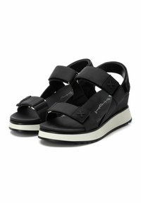 Sandalias de cuña negras con correas anchas y detalles de hebilla. Cuentan con una suela gruesa blanca y una parte superior texturizada, diseñadas para mayor comodidad y soporte.
