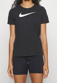Camiseta negra de manga corta Nike con logo swoosh blanco, combinada con pantalones cortos negros. Hecha de tela suave, con un corte estándar.