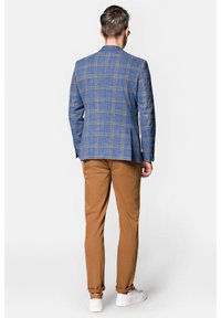 Niebieska marynarka w kratę z dwoma tylnymi wentylami, w połączeniu z brązowymi chinosami i białymi trampkami. Dopasowany krój z klasycznymi klapami i guzikiem na mankietach.