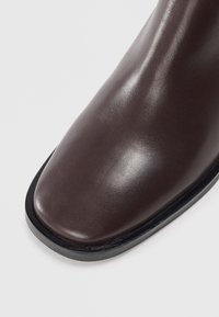 Brown leather ankle boot featuring a rounded toe, smooth surface, and a contrasting black sole. No visible patterns or hardware accents.