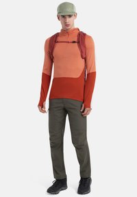 Maglietta a maniche lunghe a blocchi di colore arancione e rosso, con zip, abbinata a pantaloni cargo verde oliva e scarpe da trekking nere.