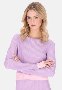 Hellvioletter gerippter Pullover mit langen Ärmeln und einem pinkfarbenen, gerippten Bund. Der Stoff hat einen subtilen Glanz, der Textur und Tiefe erzeugt.