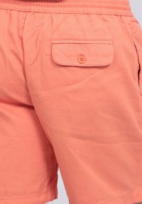 Shorts en coton couleur pêche avec une taille élastique, dotés d'une poche arrière à rabat avec fermeture à bouton et de poches latérales.
