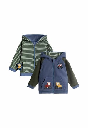 To små børnejakker med hætte, den ene stribet grøn med blå kant og en lille lastbil-patch, den anden blå med mørke ærmer og traktor patches på front og ærme.