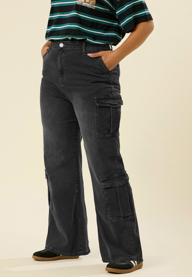 Mustat cargo-housut leveällä lahkeella, joissa on useita sivutaskuja, korkea vyötärö ja sileä pinta. Yhdistetty raidalliseen toppiin.