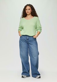 Hellgrüner, gestrickter Pullover mit V-Ausschnitt, kombiniert mit weit geschnittenen, blauen Jeans aus Denim. Die Jeans verfügen über ein klassisches Fünf-Taschen-Design.