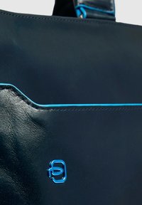 Marineblaue Ledertasche mit glatter Textur, kontrastierenden blauen Nähten und einem Logodetail. Minimalistisches Design mit schlanker Silhouette.