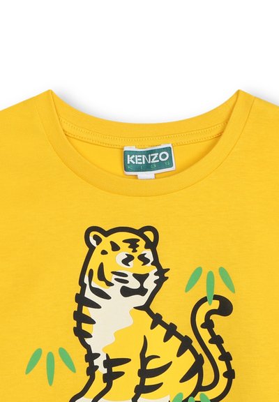 T-shirt di cotone giallo con una grafica di tigre contornata in nero, con accenti gialli e bianchi, e elementi di bambù verdi attorno.