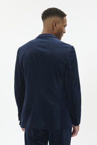 Meresinise sametist ülikonnajakk struktuurse disainiga, tagant ühe läbilõikega, kahe nupuga ja siledapinnaline. Lõigatud sobivuses.