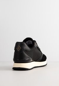 Black sneaker with leather and suede materials, featuring a white sole, textured accents, and a gold logo on the heel.
