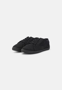 Schwarze Sneakers mit einem Obermaterial aus Canvas und einem strukturierten Seitenpanel. Ausgestattet mit runden Schnürsenkeln und einer Gummisohle. Niedrigprofi-Design.