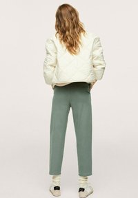 Giacca bomber trapuntata color crema, pantaloni verdi a vestibilità rilassata, sneakers bianche e calzini color crema. Presenta un design corto e una texture morbida.