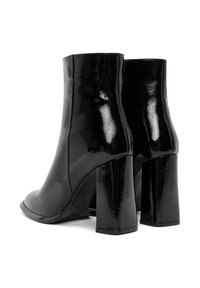 Botines negros hasta el tobillo con un acabado brillante, tacón cuadrado alto y forma estilizada. Presenta una textura suave y un diseño minimalista.