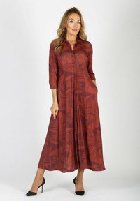 Czerwona sukienka z długim rękawem, ozdobiona wzorem liści, zapinana na guziki, z bocznymi kieszeniami i zwiewnym krojem, zestawiona z czarnymi szpilkami.