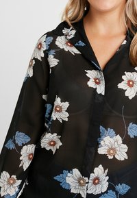 Sort gennemsigtig bluse med blomstermønster, der har hvide og blå blomster. Har en krave og knaplukning foran. Blød tekstur med løs pasform.