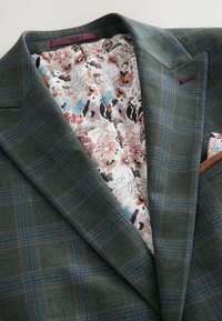 Grønternet blazer med en tekstureret uldoverflade. Foret med blomstret stof i pink, blå og sorte nuancer.