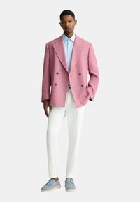 Blazer rosa doppiopetto con motivo a quadri, camicia azzurra chiara, pantaloni bianchi e scarpe azzurre chiare, con una vestibilità rilassata.