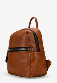 Mochila de imitación de cuero marrón con forma redondeada, que cuenta con un bolsillo frontal con cremallera, herrajes en tono dorado y un pequeño asa en la parte superior.