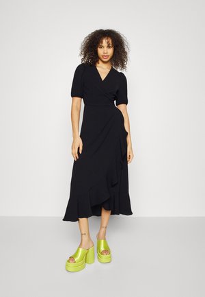 Black wrap dress with short puff sleeves, a ruffled hem, paired with bright green platform sandals with a thick sole.