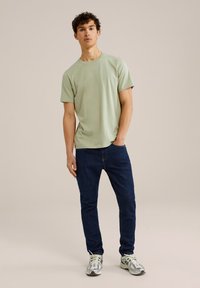 Šviesiai žalias trumpas rankovėmis marškinėliai derinami su tamsiai mėlynomis džinsais ir pilkais sportbačiais. Apranga pasižymi laisvalaikio dizainu ir patogiu prigludimu.