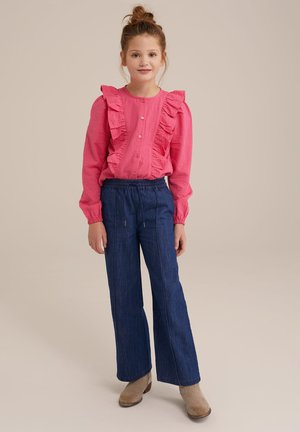 Rosa gerippte Bluse mit Rüschen, Knopfleiste und langen Ärmeln, kombiniert mit blauen weit geschnittenen Jeanshosen. Stiefel vervollständigen das Outfit.